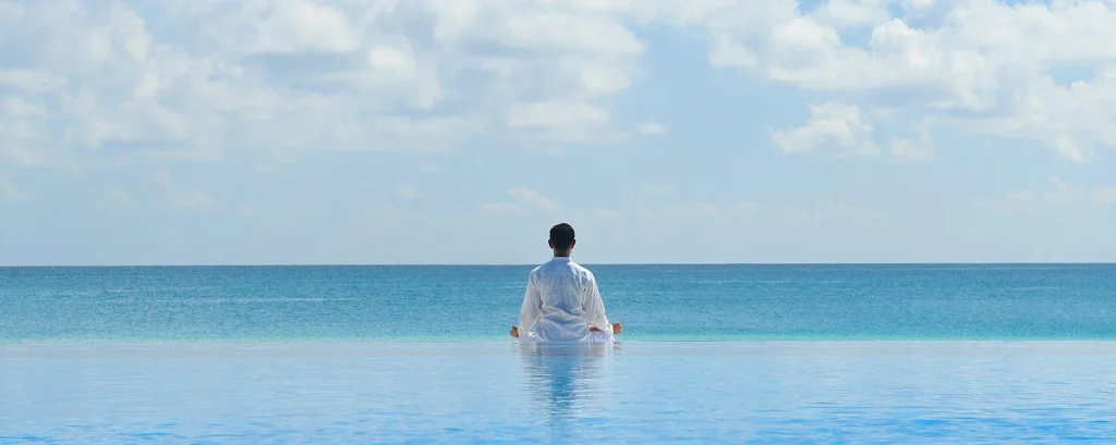 فردی با لباس سفید درساحل آبی دریا در حال رسیدن به آرامش درونی