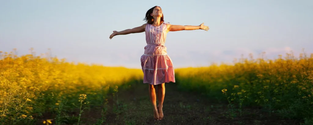 دختری با دستانی باز در دشتی سبز حس آزادی را با حضور در لحظه حال تجربه می‌کند